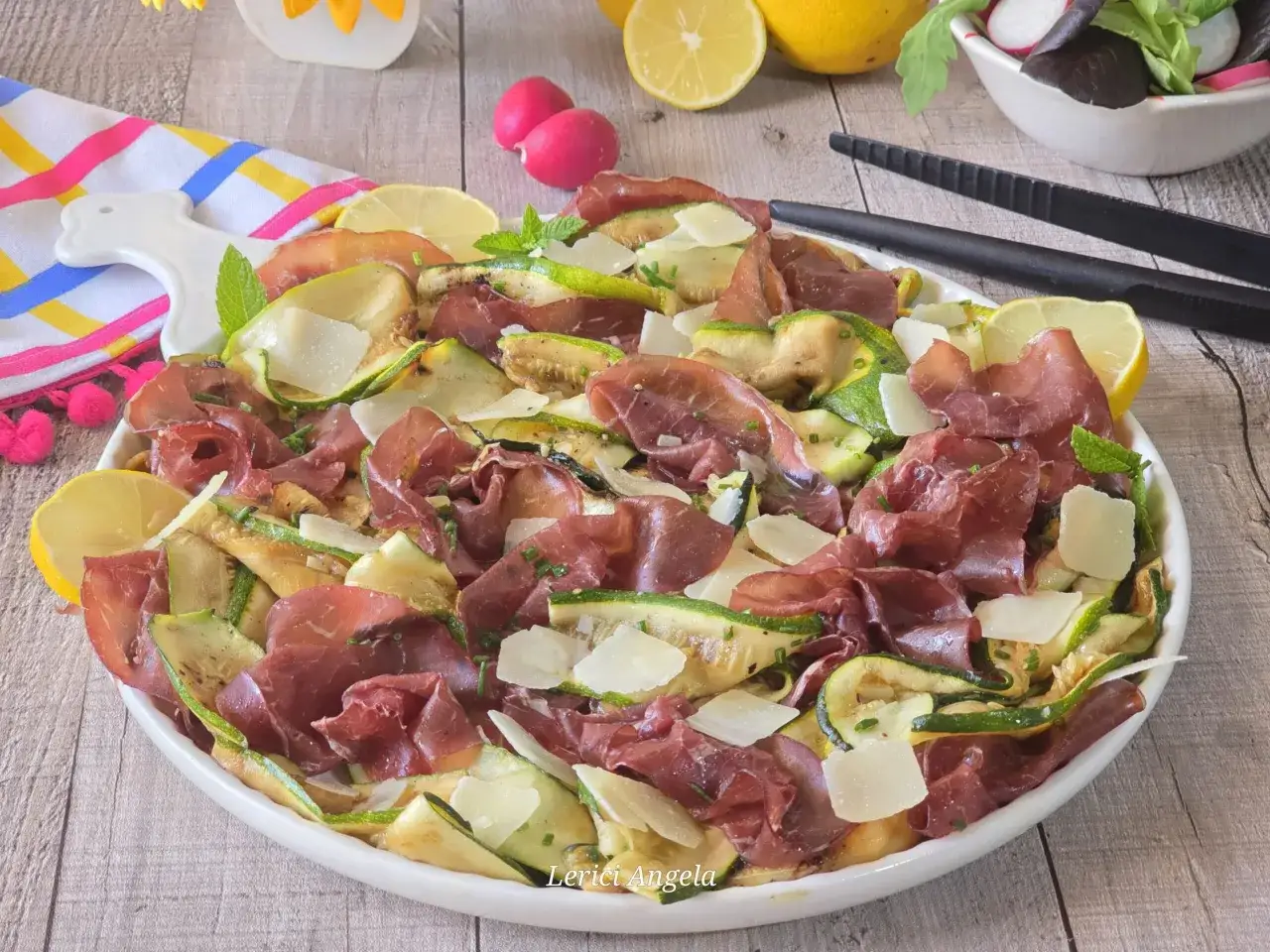 Deliziosa insalata di zucchine grigliate, arricchita da fette di bresaola, scaglie di parmigiano e spicchi di limone.