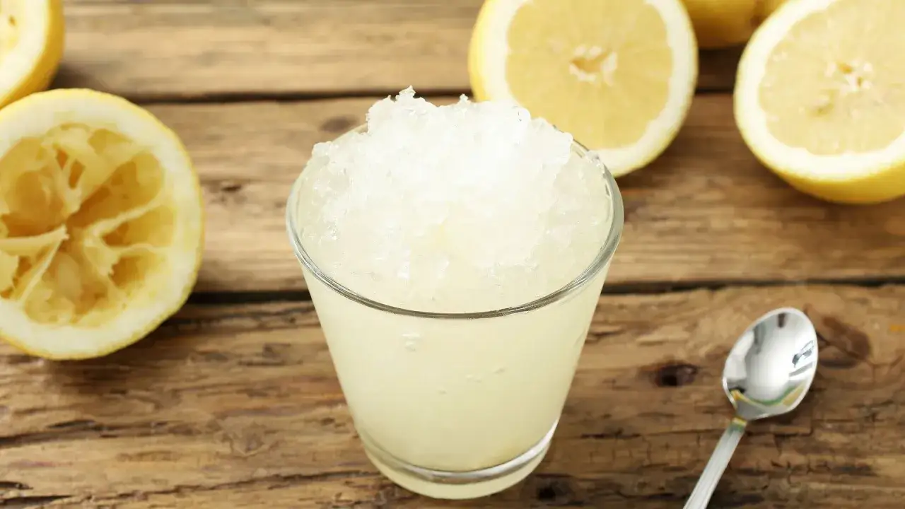 Refrescante granizado de limón, perfecto para un día caluroso. Limones frescos y una cuchara lista para disfrutar.