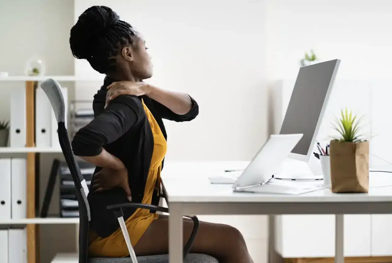 Femme se tenant le dos et l'&eacute;paule, souffrant de douleurs dues &agrave; une mauvaise position bureau.