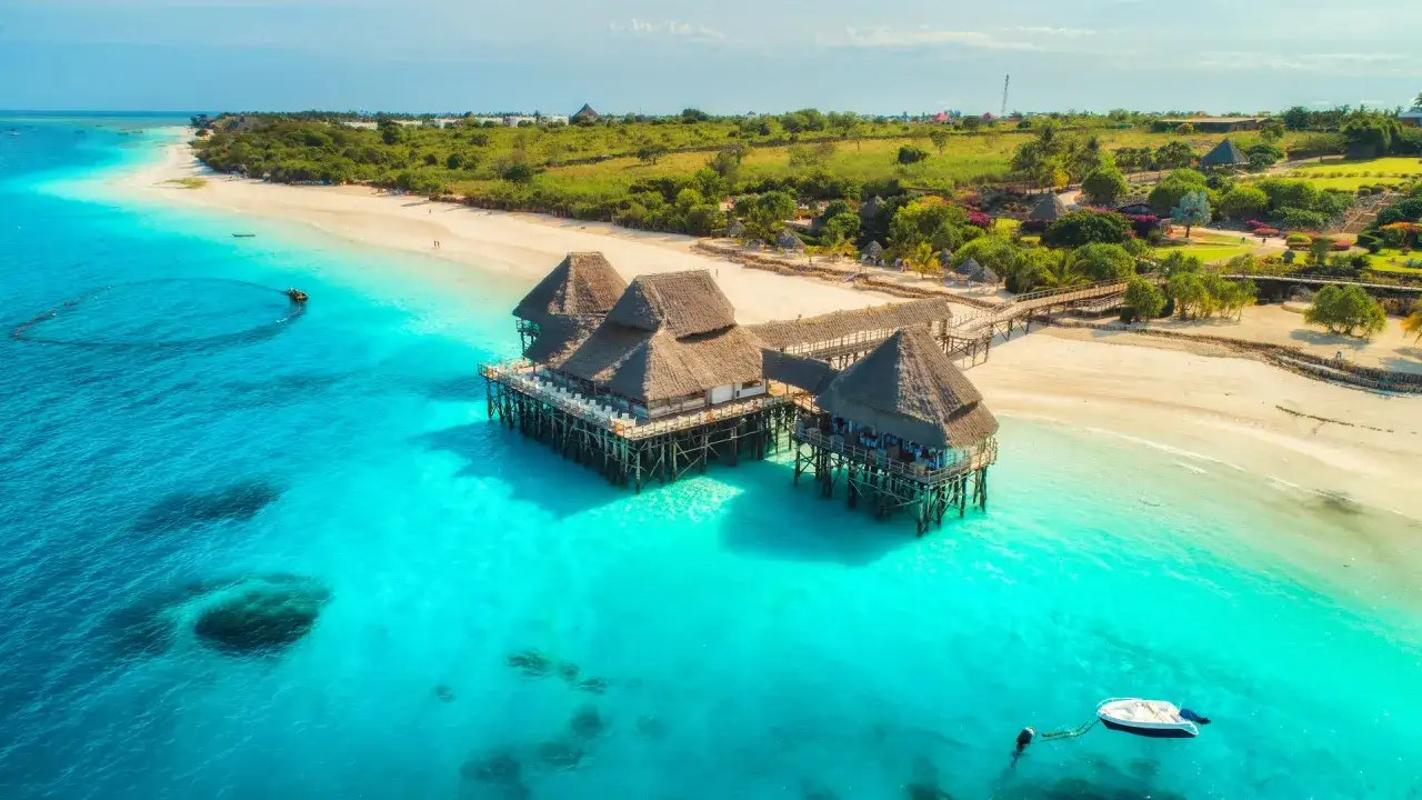 Zanzibar wycieczki fakultatywne: domki na palach nad turkusową wodą, biała plaża i bujna zieleń. Idealne miejsce na relaks.