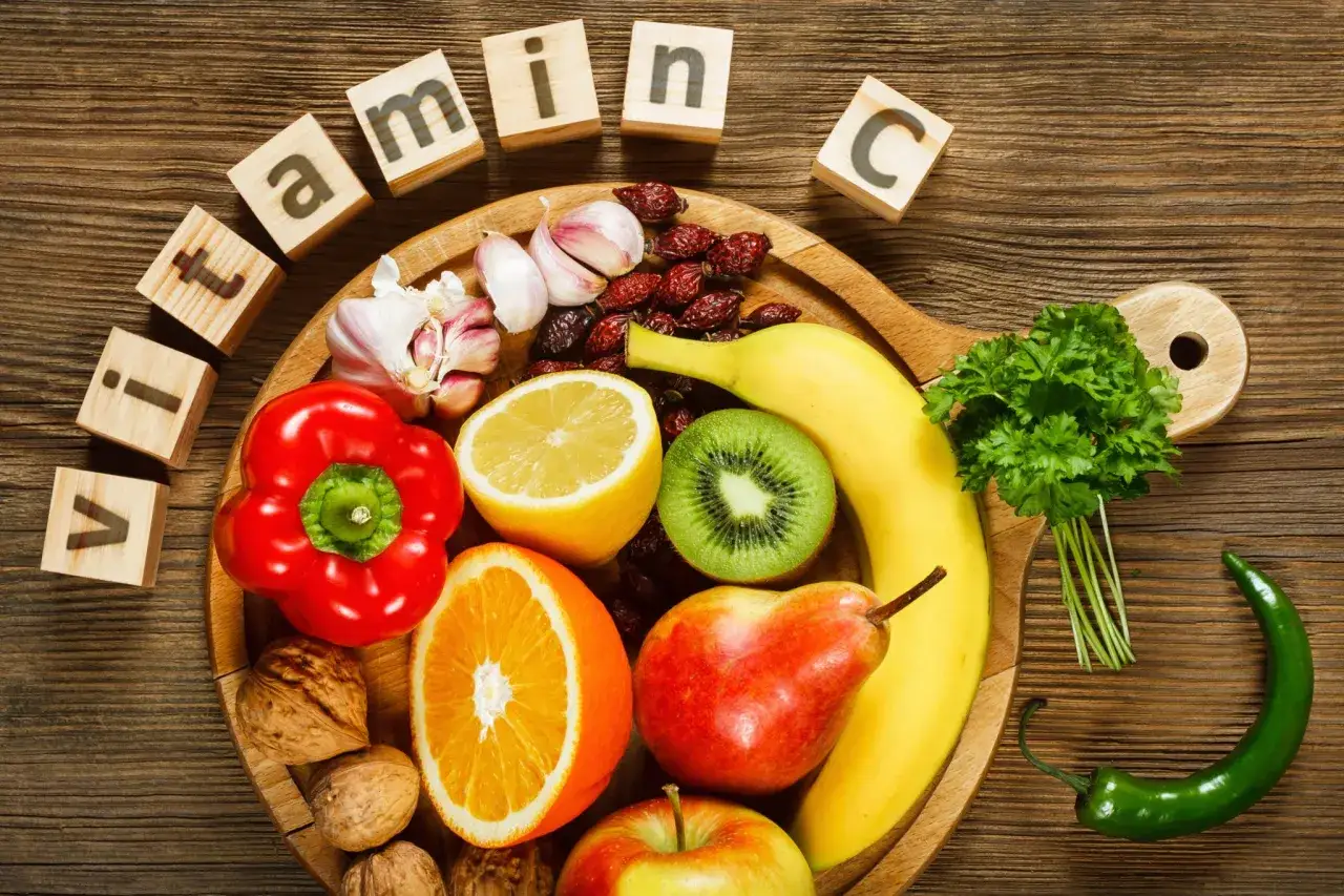 Owoce i warzywa na desce: papryka, pomarańcza, cytryna, kiwi, banan, gruszka, jabłko, orzechy, czosnek, dzika róża, papryczka chili i natka pietruszki. Co ma najwięcej witaminy C?