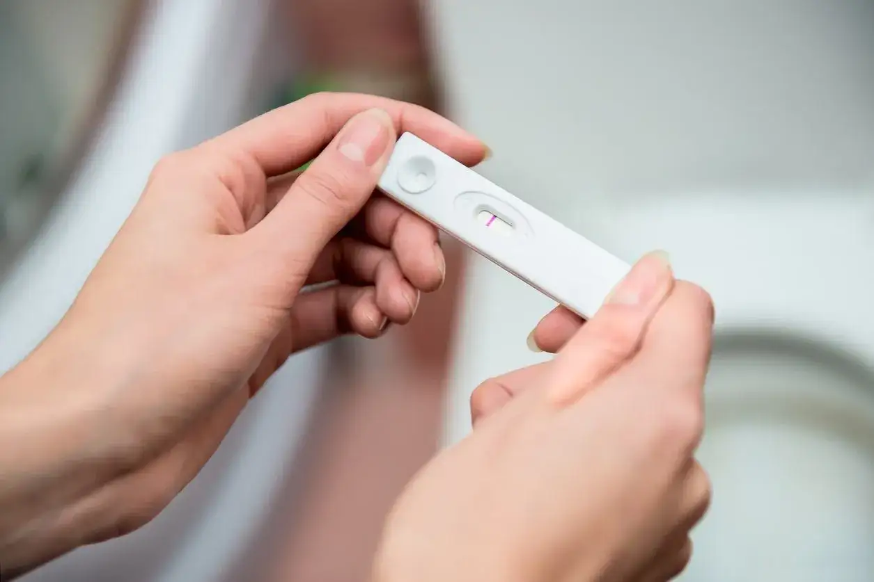 Dwie dłonie trzymają test ciążowy z widocznym jednym paskiem. Widać niepewność i strach przed ciążą po stosunku.