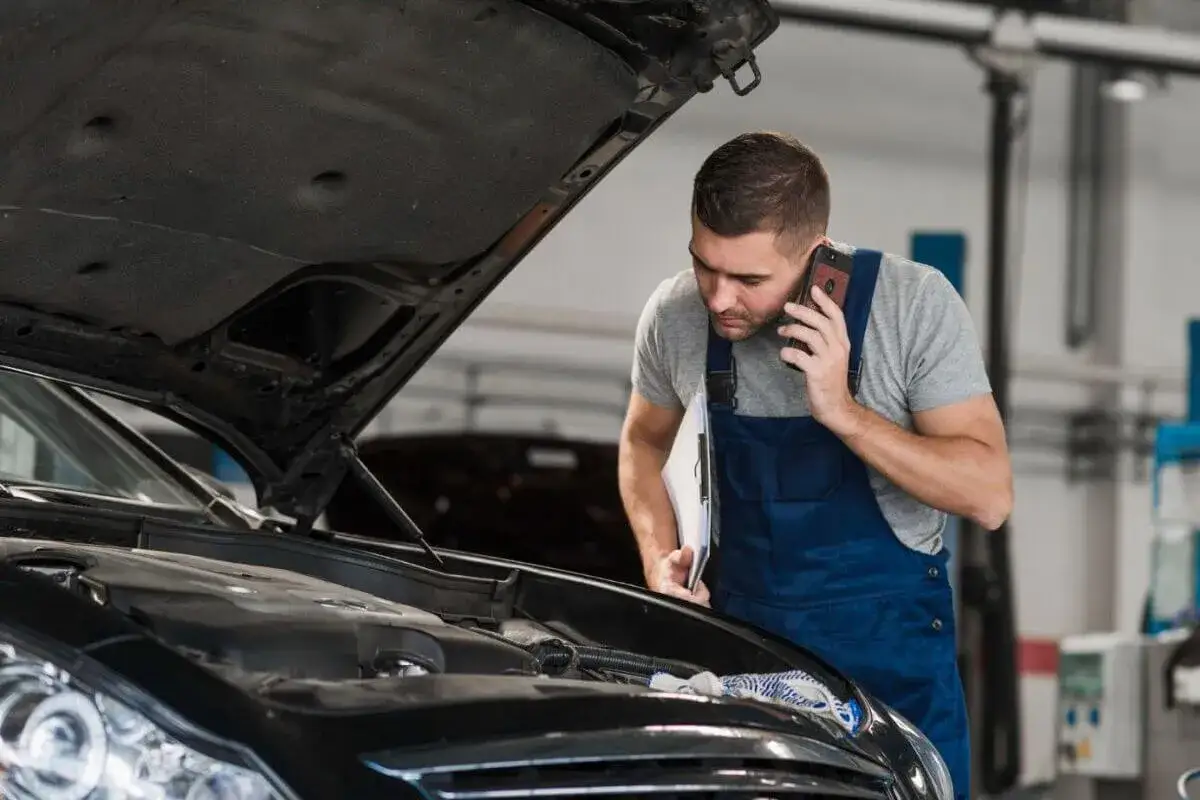 Mechanik zaniepokojony skutkami pomylenia oleju silnikowego z olejem do skrzyń ATF, rozmawia przez telefon przy otwartej masce samochodu.