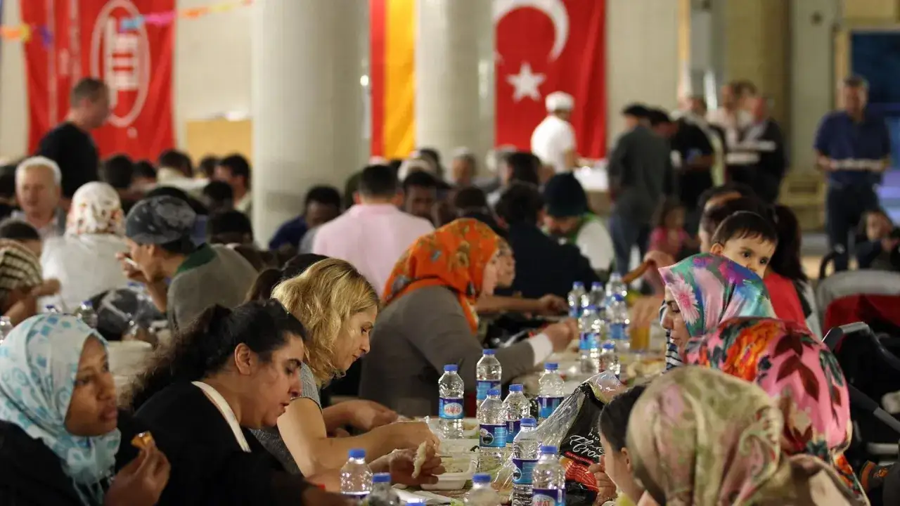 Menschen sitzen an langen Tischen, essen und trinken. Fahnen im Hintergrund, darunter die t&uuml;rkische. Ein Festessen, vielleicht nach dem Fasten.