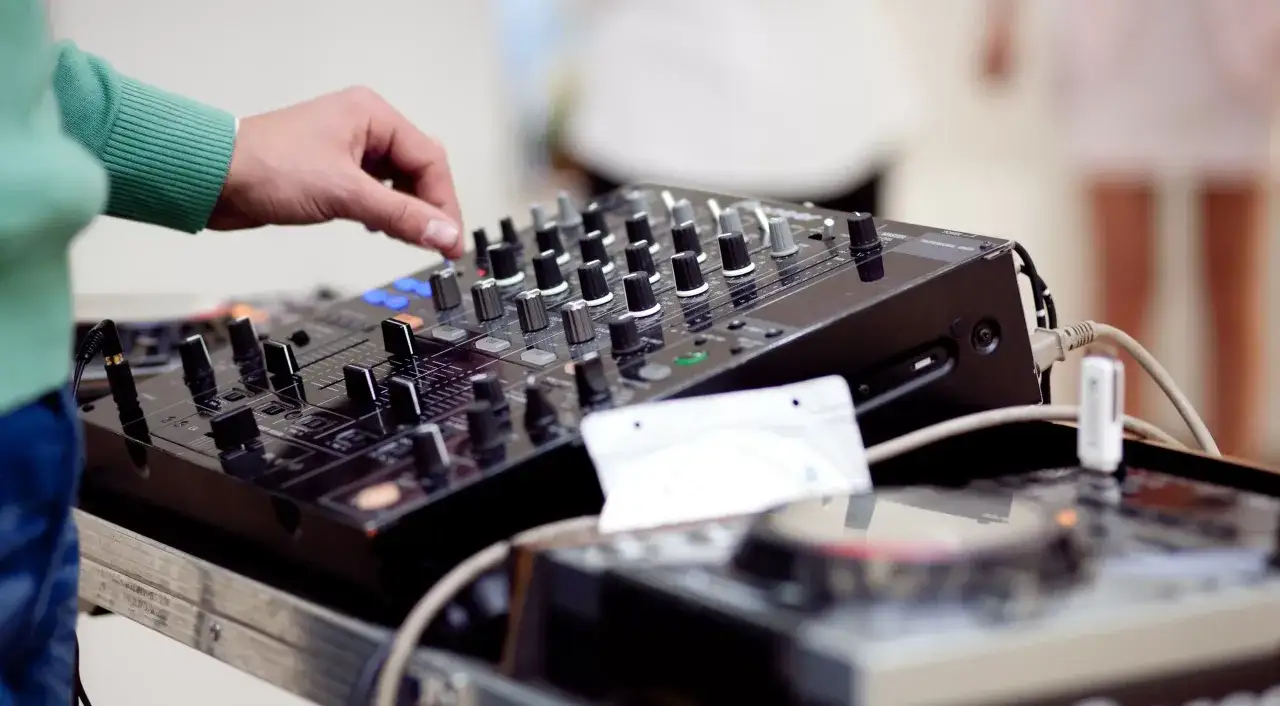 Main d'un DJ manipulant les boutons d'une table de mixage, la meilleure interface audio pour créer une ambiance festive.