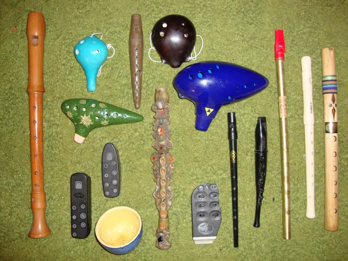 Kolekcja instrumentów dętych: drewniana **flauta**, niebieska i zielona ocarina, ciemnobrązowa ocarina, niebieska ocarina w kształcie stworka, ozdobna fletnia Pana, kilka mniejszych fletów i bambusowy flet.