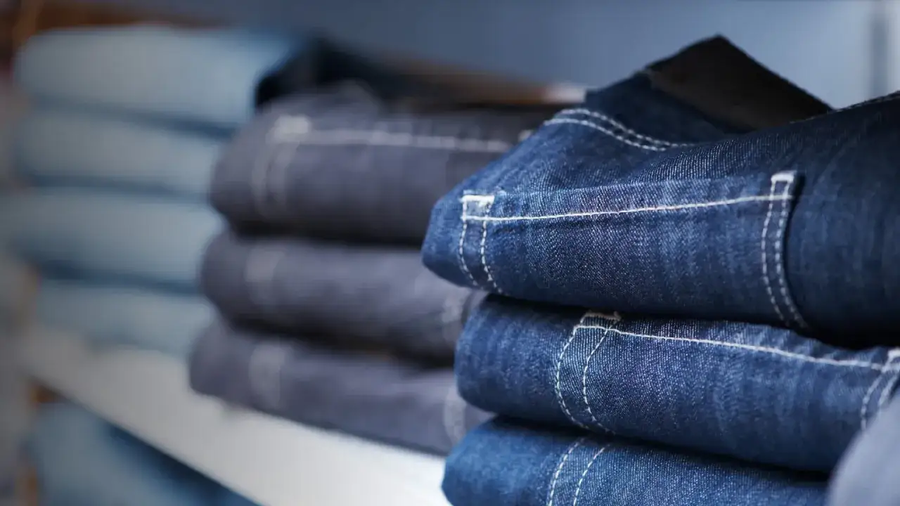 Pila de pantalones vaqueros de **denim material** con costuras blancas visibles.