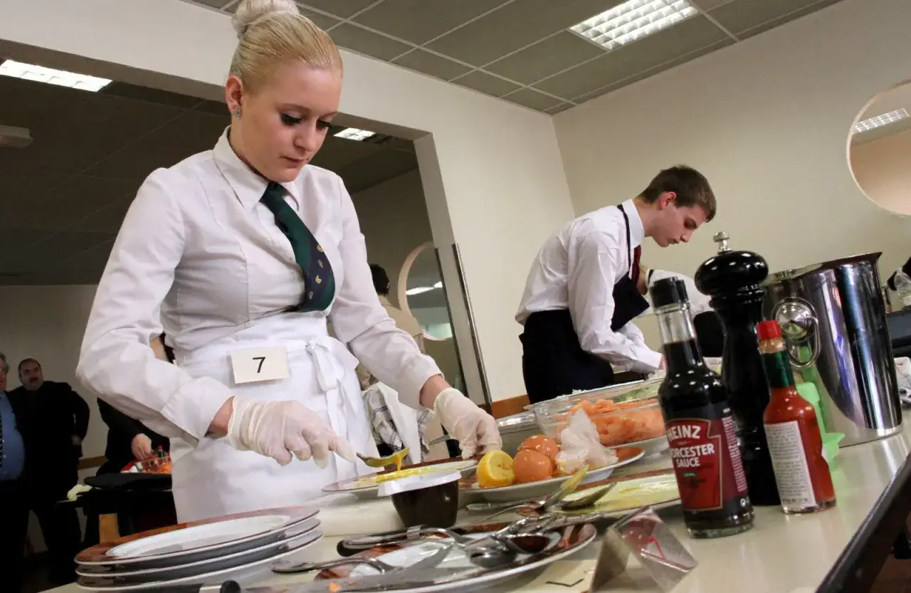 Jeune femme en tablier blanc préparant une cuisine faite maison. Un homme en arrière-plan travaille également.