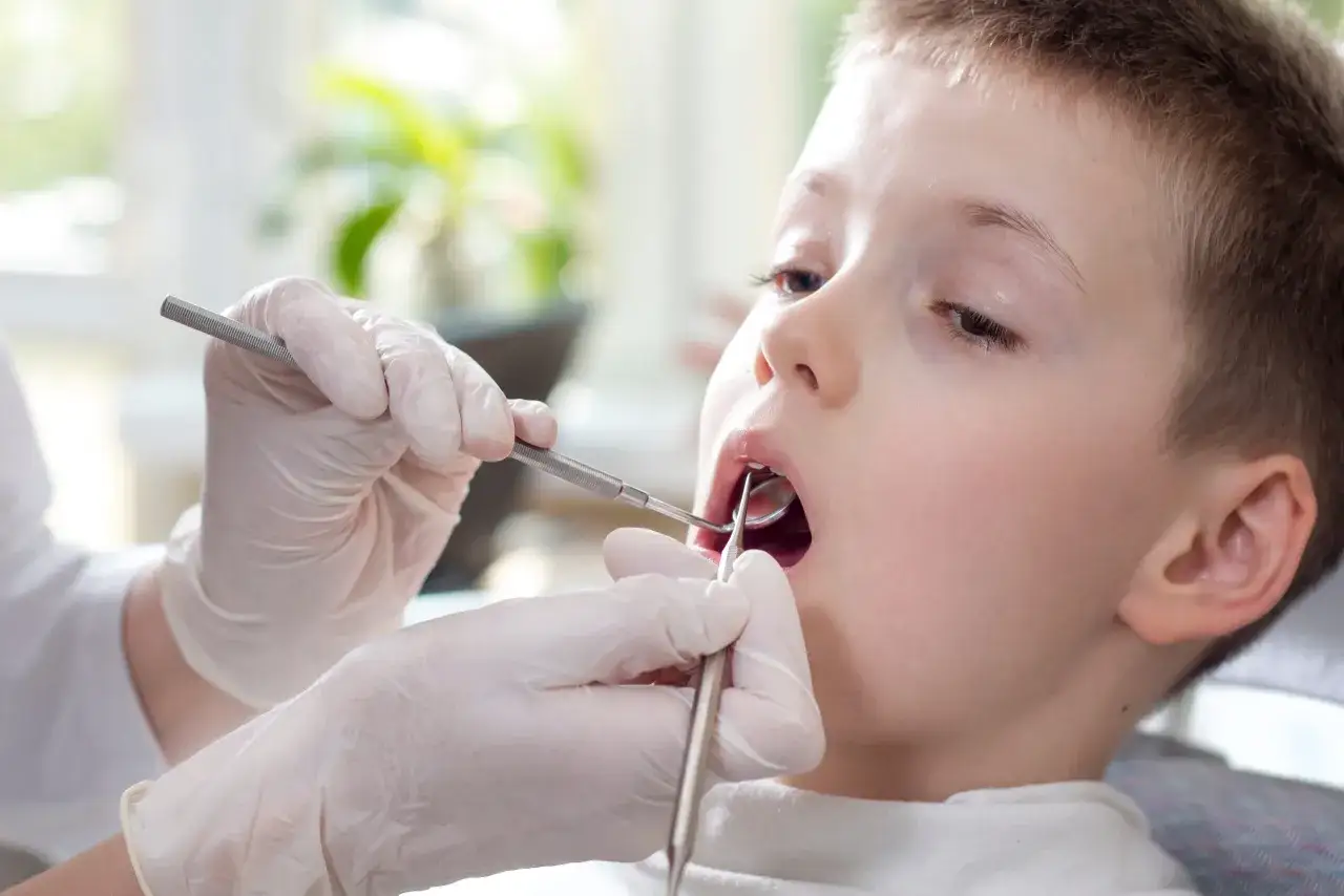Chłopiec przechodzi zabieg lakowania zębów. Dentysta w rękawiczkach używa narzędzi do ochrony jego uśmiechu.