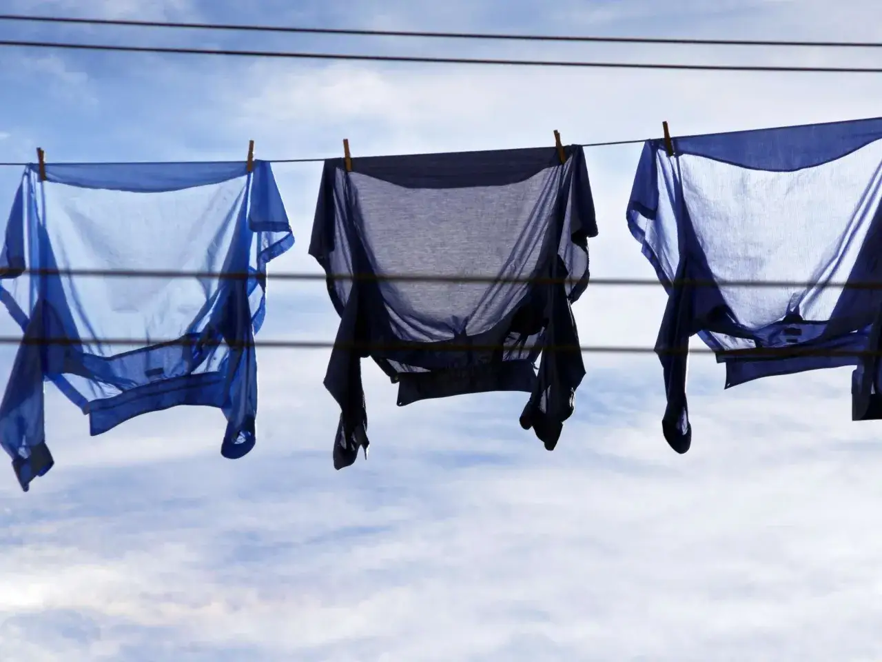 Drei blaue Hemden trocknen an einer W&auml;scheleine im Wind. Das frische Hemd nach dem Waschen duftet nach Sommer.