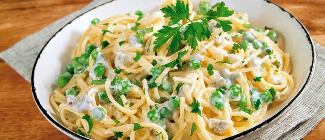 Ein Teller cremiger Pasta mit Erbsen und Petersilie. Das ist, was Fettuccine sein kann: eine k&ouml;stliche Mahlzeit.