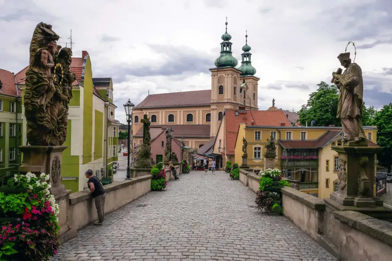 Kamienny most z rzeźbami i barokową architekturą, w tym kościołem z zielonymi wieżami. To piękne ziemia kłodzka atrakcje.