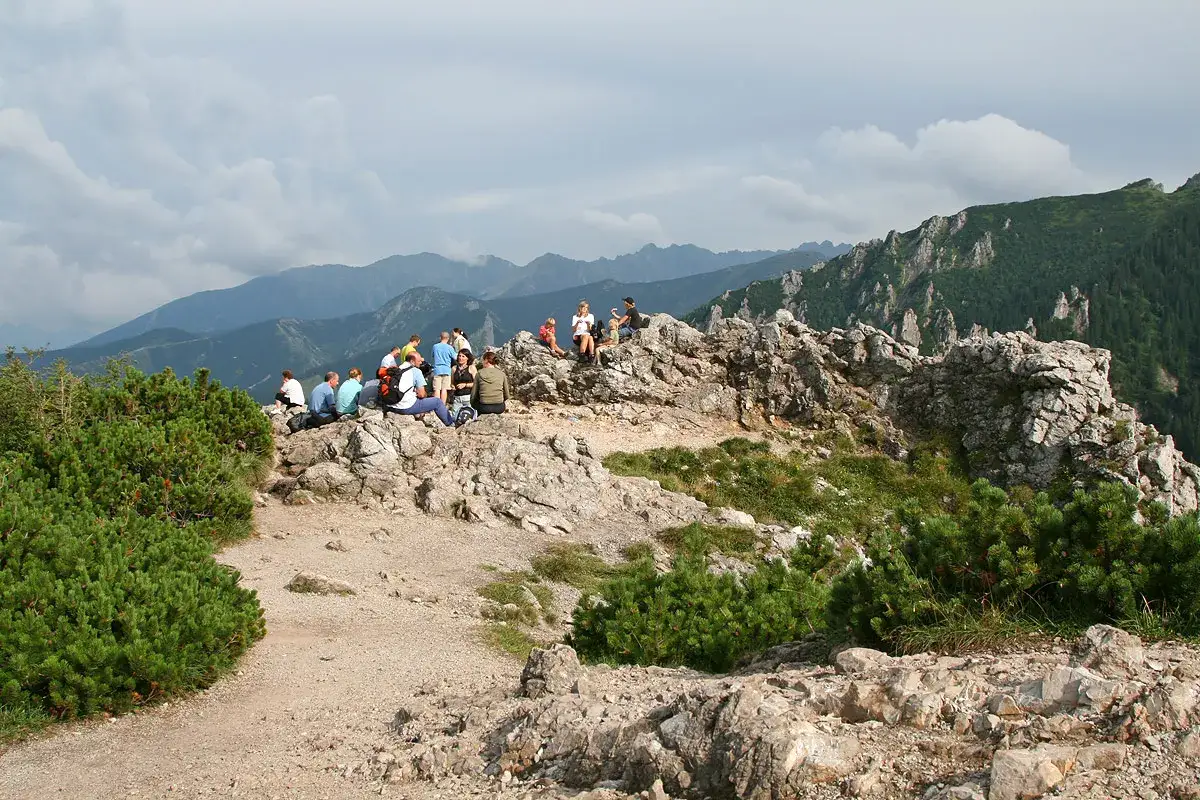 Grupa turystów odpoczywa na skalnym szczycie w Dolinie Strążyskiej, podziwiając widok na Tatry z okolic Sarniej Skały.