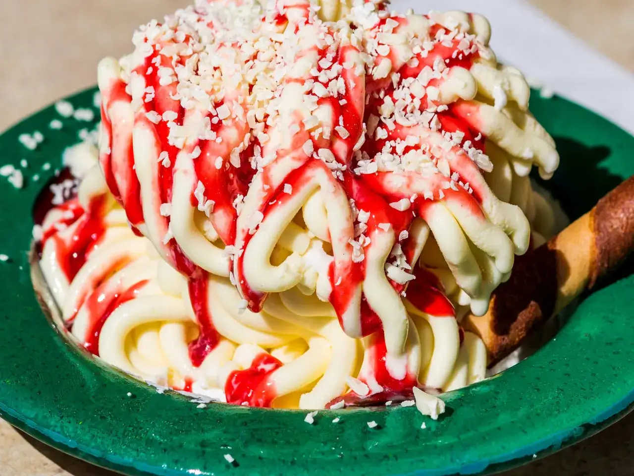 Ein leckeres Spaghetti-Eis mit Erdbeersauce und weißen Schokostückchen in einer grünen Schale.