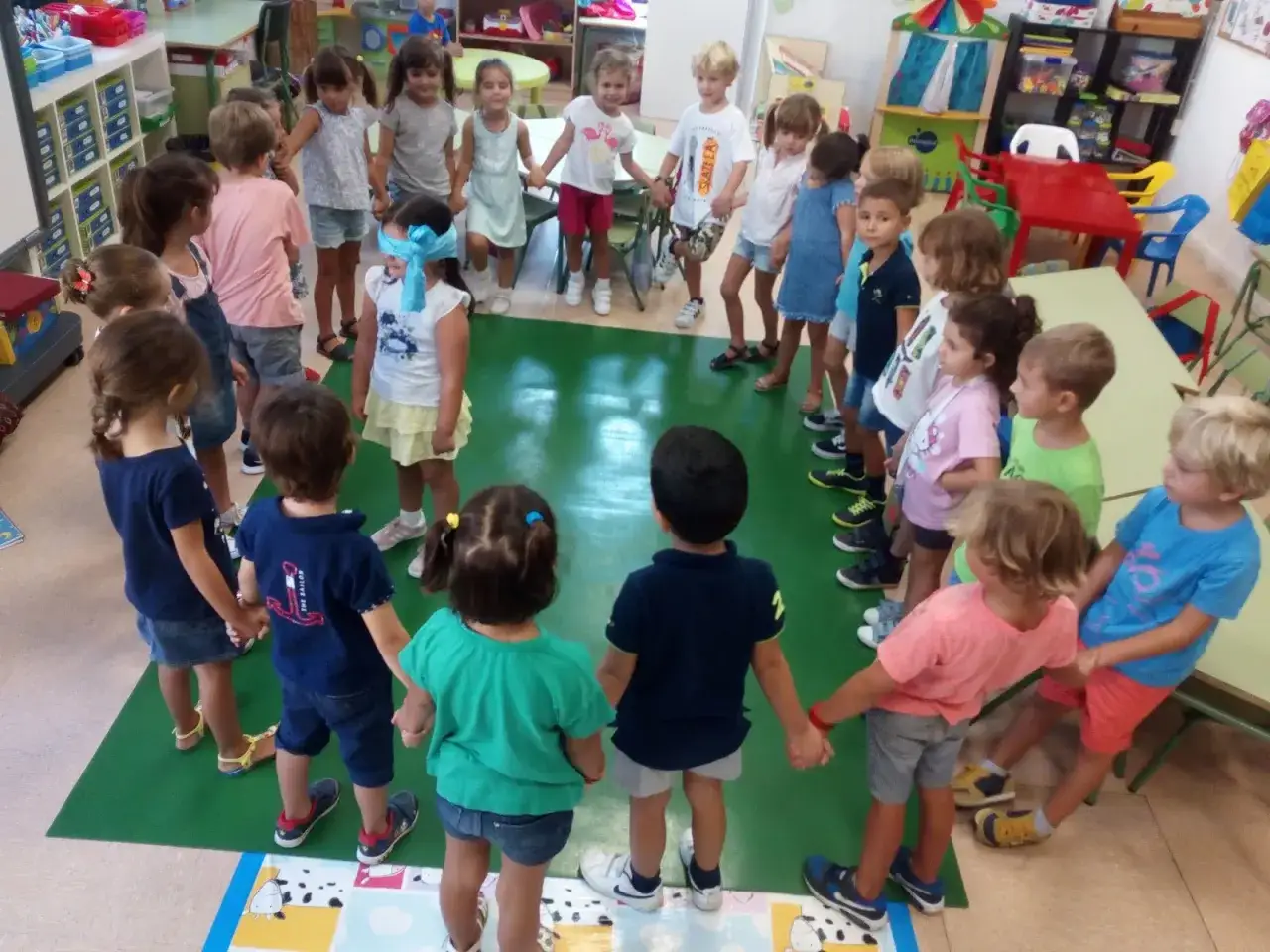 Ni&ntilde;os de 3 a 4 a&ntilde;os en el colegio jugando a la gallinita ciega en c&iacute;rculo, tomados de la mano.