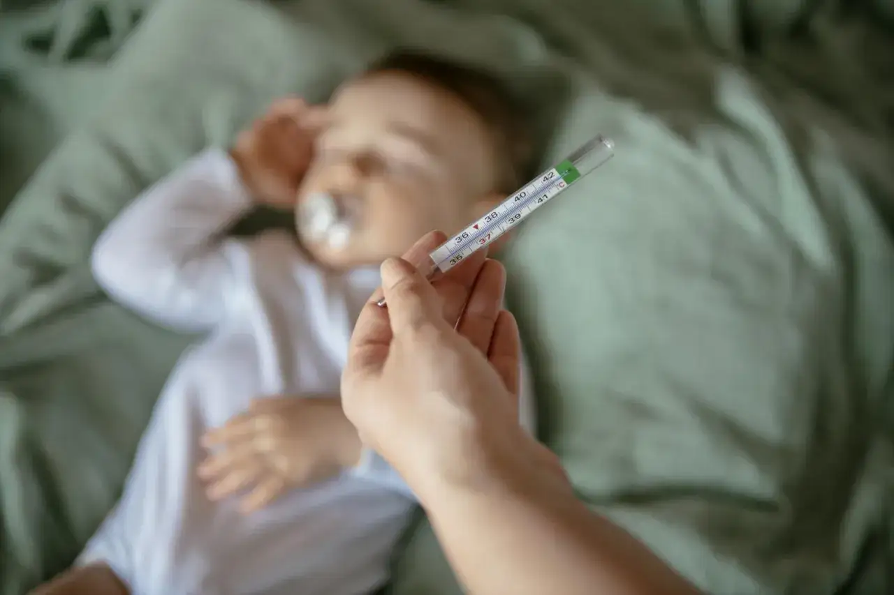 Dłoń trzyma termometr przy śpiącym dziecku. Czyżby to był kichanie u noworodka?