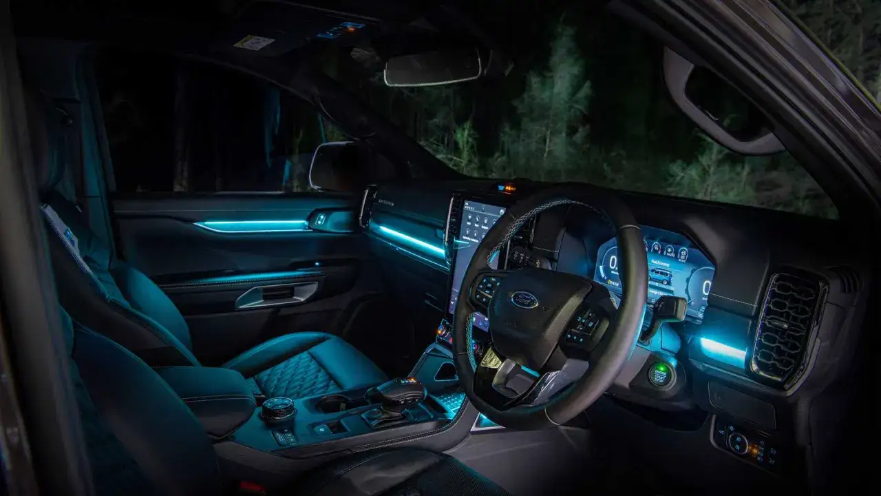 Wnętrze Ford Everest nocą, oświetlone niebieskim nastrojowym światłem. Skórzane fotele i nowoczesny kokpit tworzą futurystyczną atmosferę.