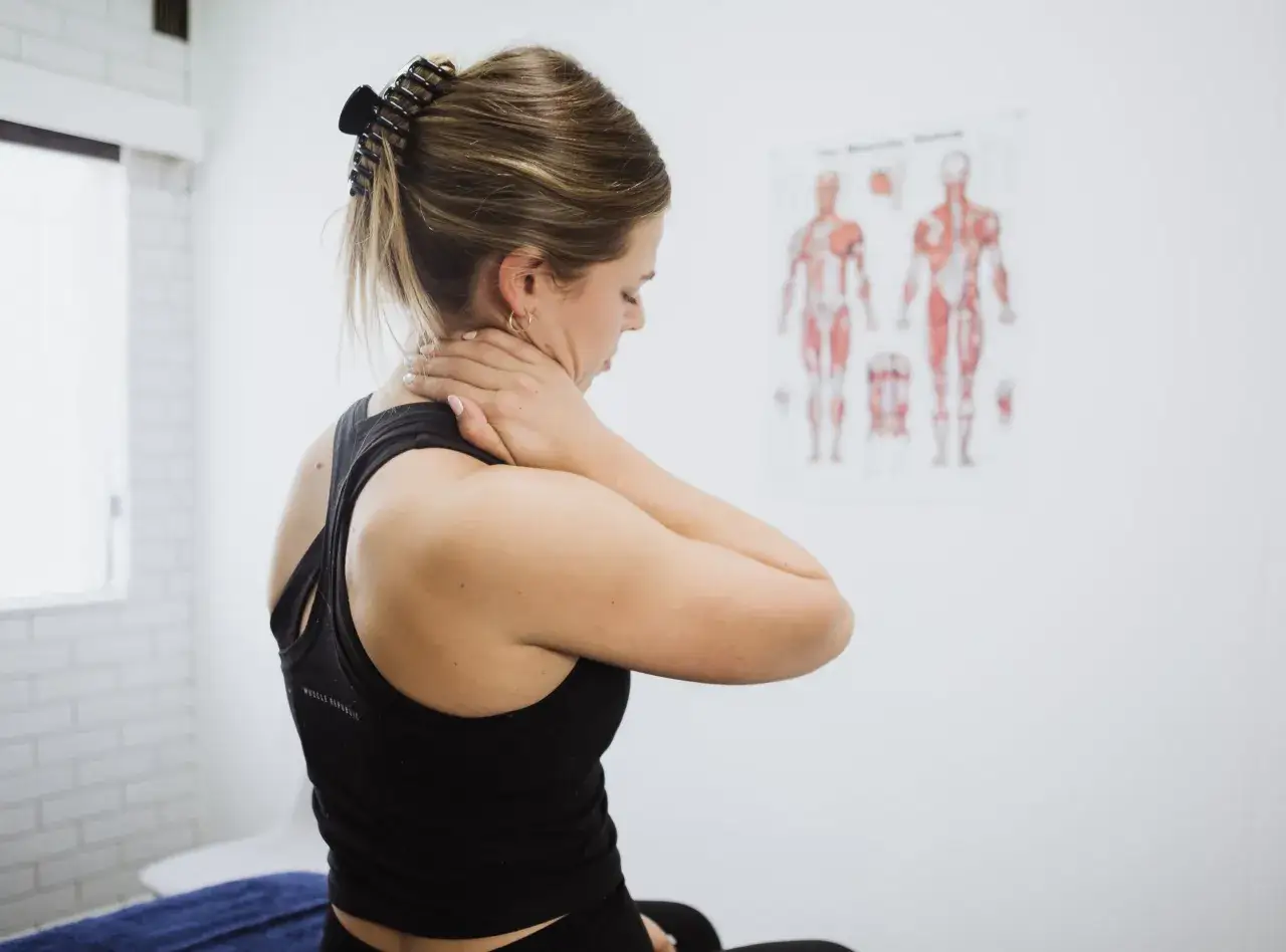Donna con dolore cervicale si massaggia il collo, in attesa di un osteopata cervicale.