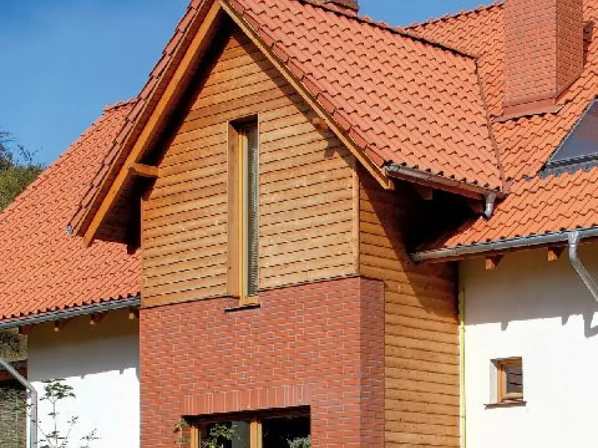 Nowoczesny projekt elewacji starego domu: czerwona dachówka, drewniane panele i cegła tworzą harmonijną całość.