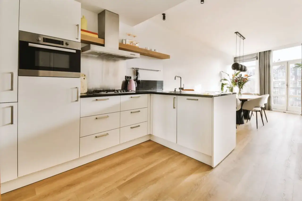 Cocina moderna con armarios blancos y encimeras negras. El suelo de madera clara complementa perfectamente los suelos para cocinas blancas, creando un ambiente luminoso y acogedor.