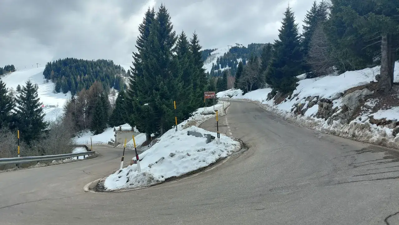 Strada innevata verso il Monte Bondone. Cosa fare? Godersi il panorama invernale e le piste da sci in lontananza.