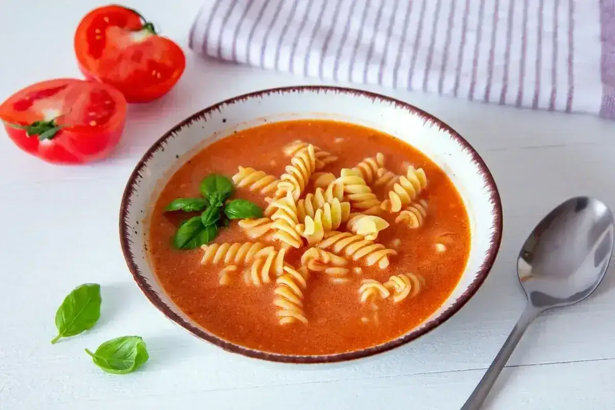 Miseczka pomidorowej z makaronem fusilli, świeżą bazylią i pomidorami. Idealne przyprawy do zupy pomidorowej podkreślają smak.
