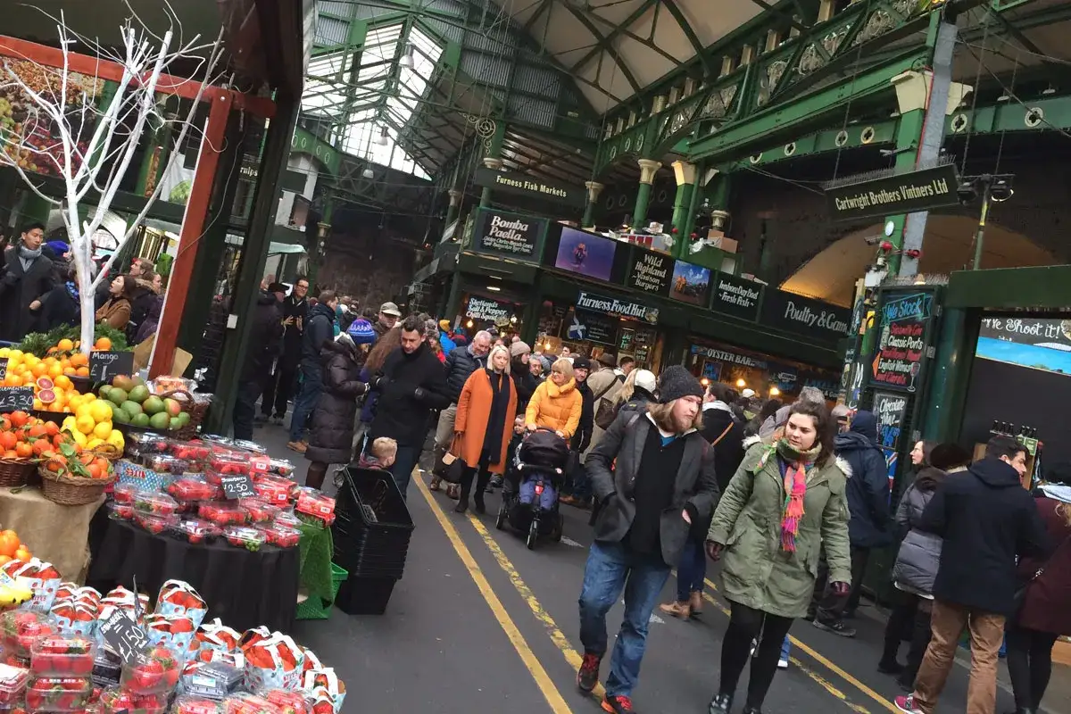Bunte Obststände und geschäftige Menschenmengen in einer Markthalle. Ein toller Ort, um zu sehen, was tun in London.