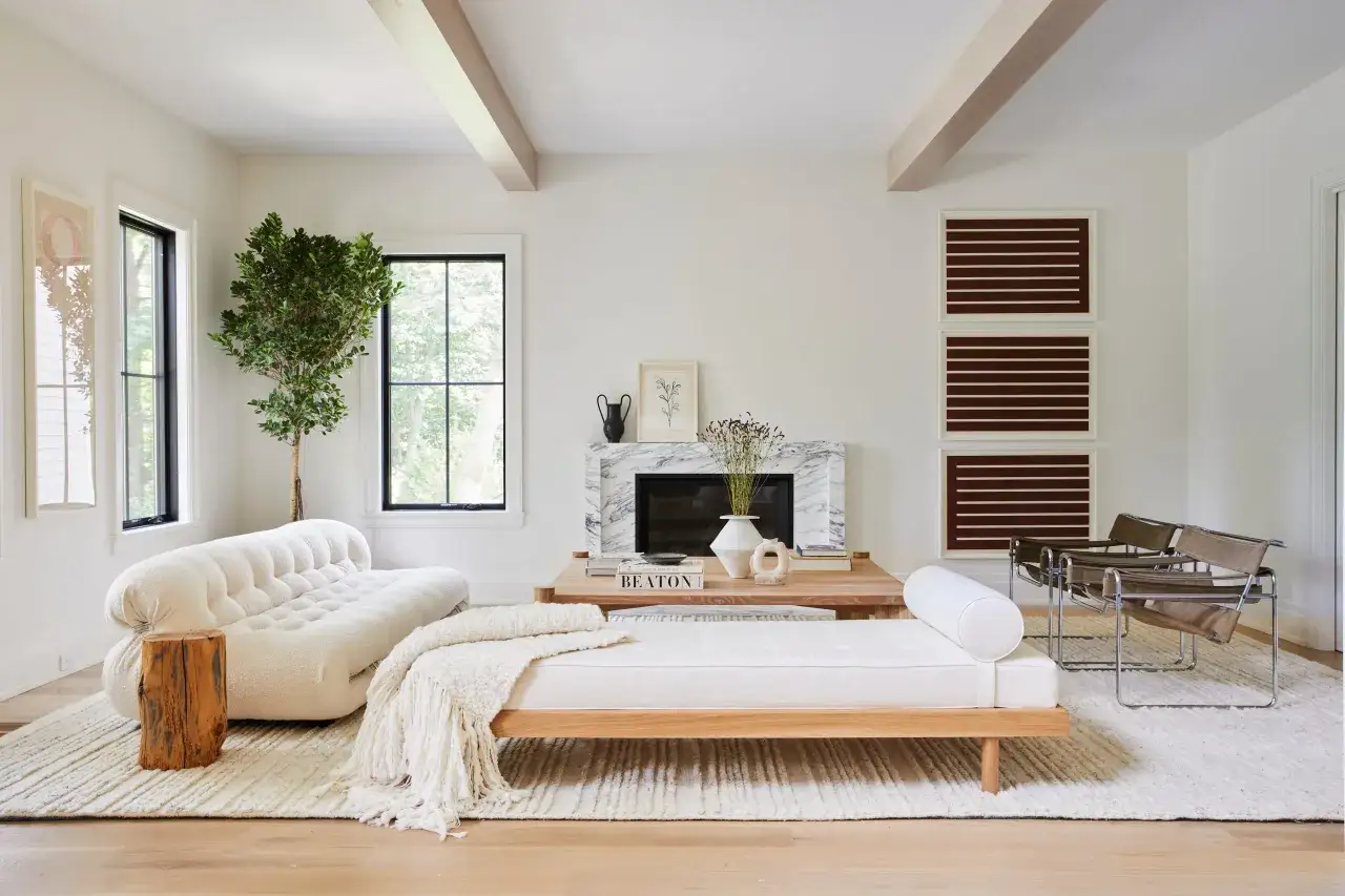 Ideas para decorar un salón con muebles blancos: sofá curvo, daybed de madera, chimenea de mármol y sillones de cuero.