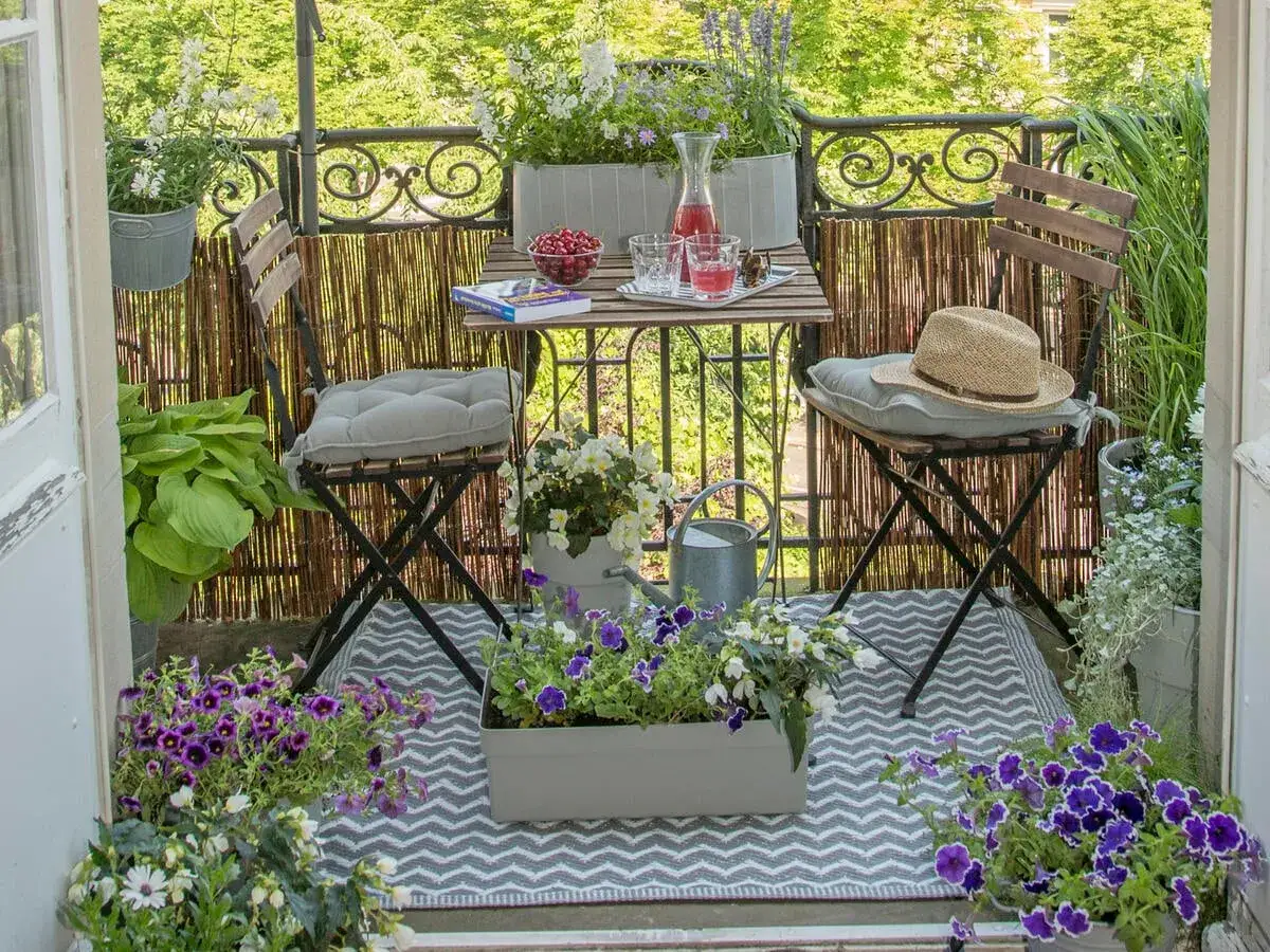 Gemütliche Balkon Ideen: Ein kleiner Tisch mit Stühlen, Blumen und einer Kanne Limonade laden zum Verweilen ein.