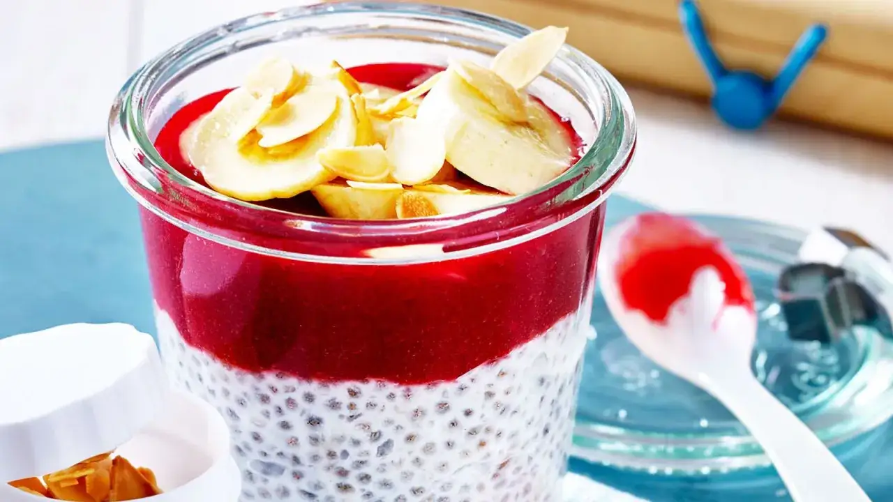 Schichtweise zubereiteter Chia Pudding mit roter Fruchtsauce, Bananenscheiben und Mandelbl&auml;ttchen.