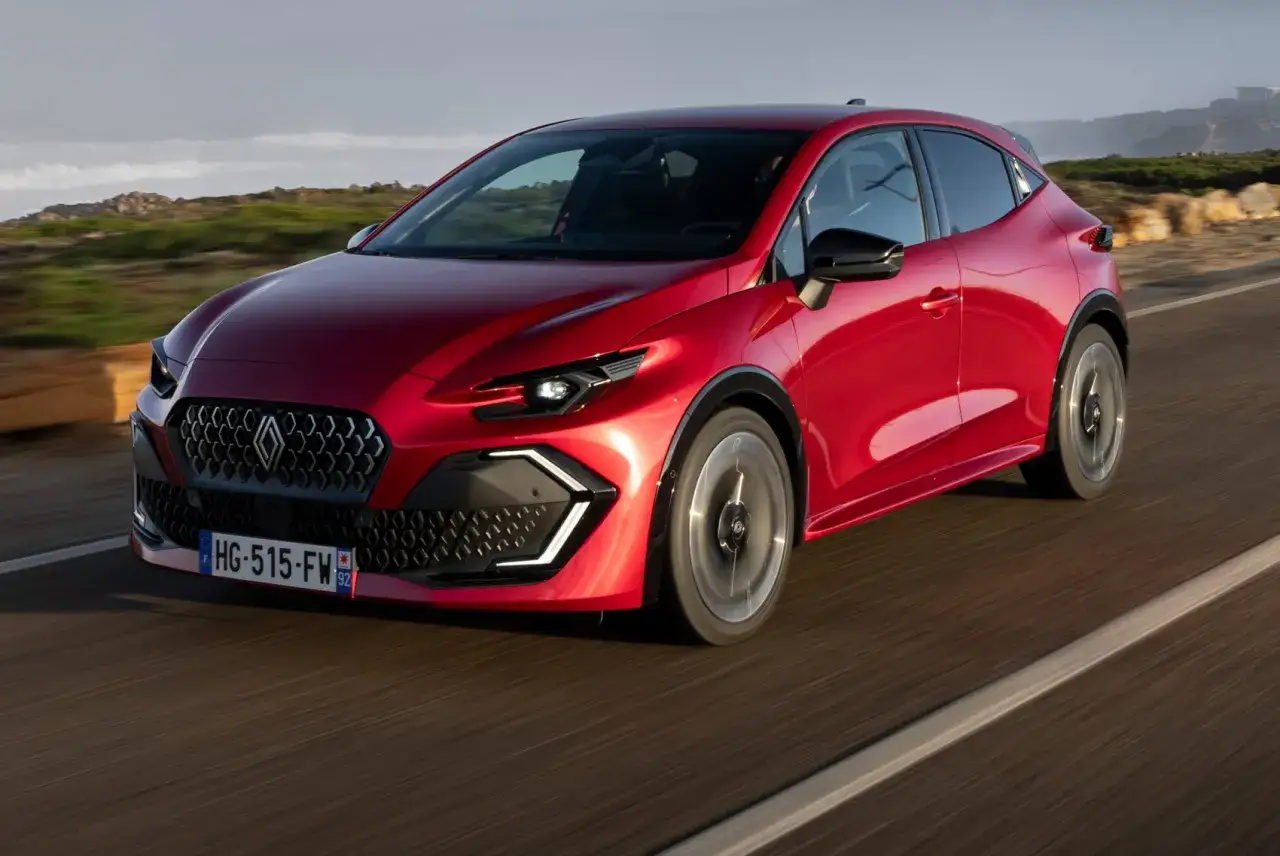 El nuevo Clio 2026, un coche rojo brillante, avanza por una carretera costera con un dise&ntilde;o moderno y deportivo.