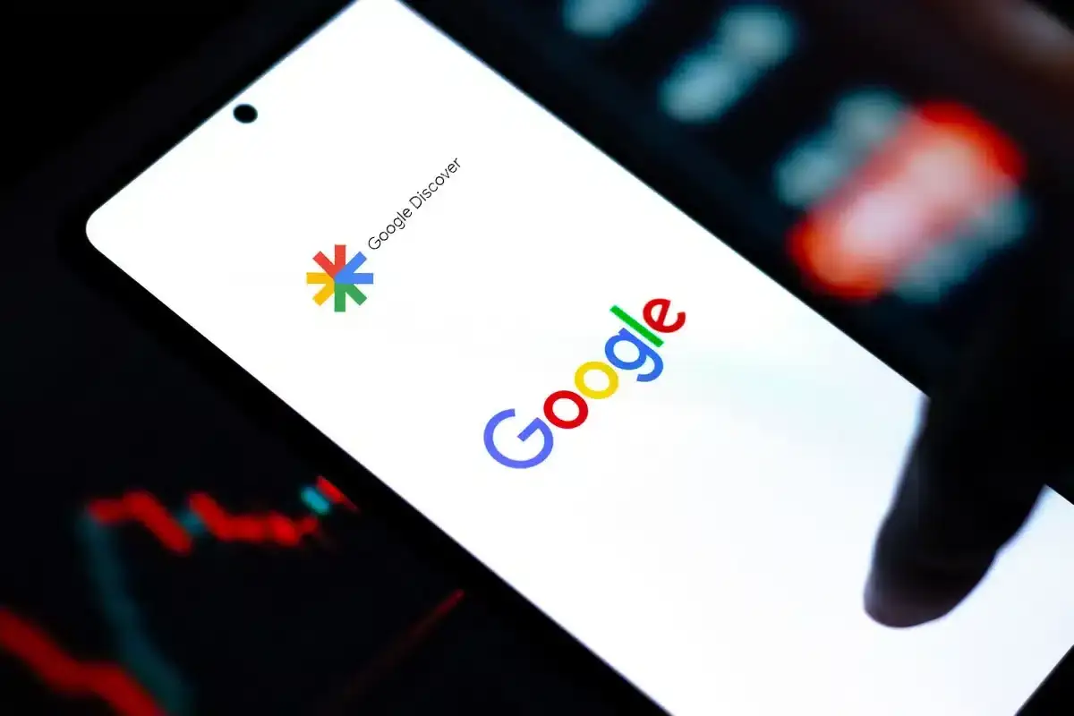 Smartfon z logo Google i napisem Google Discover. W tle wykresy giełdowe.