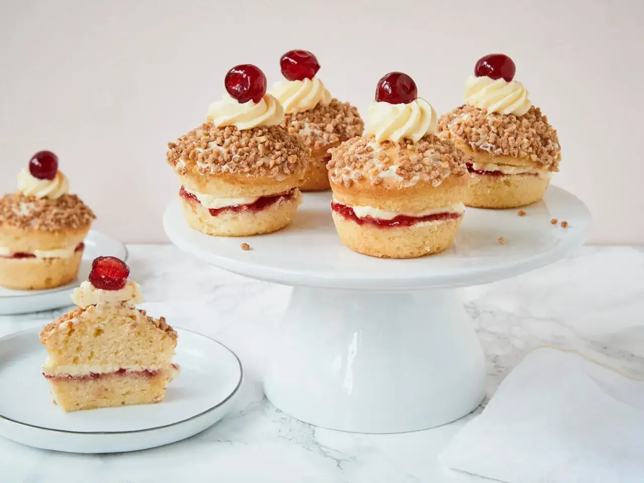 Mini-Frankfurter-Kranz-Muffins mit Buttercreme, Marmelade und Kirschen, umh&uuml;llt von knusprigen Mandelsplittern.
