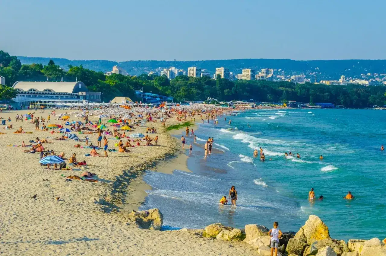 Słoneczny dzień na plaży pełnej ludzi, kolorowych parasoli i turkusowego morza. To idealne miejsce na wakacyjne atrakcje.
