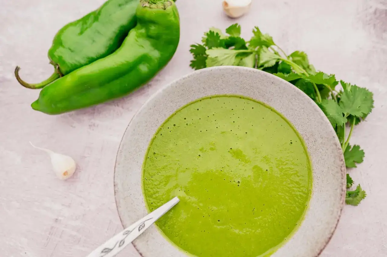 Sauce mojo verde vibrante dans un bol, avec des poivrons verts, de l'ail et de la coriandre frais à proximité.