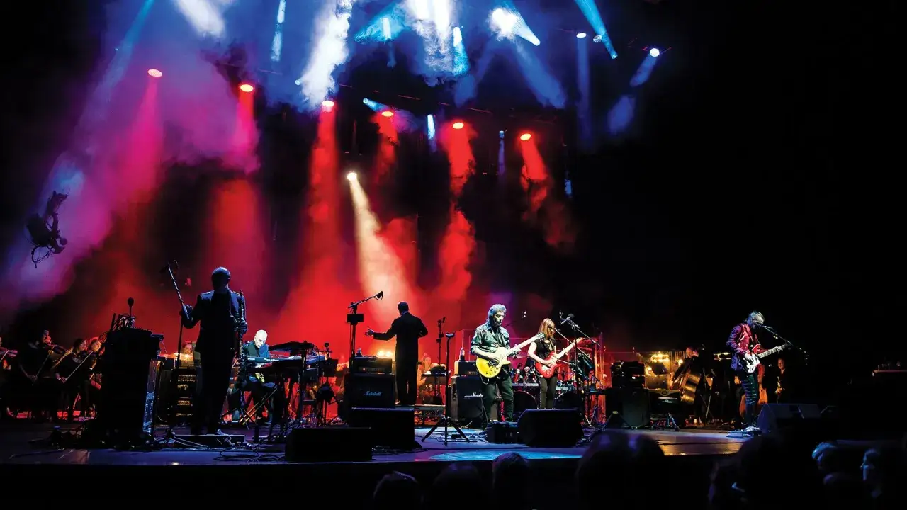 Musicians perform on a stage with red and blue lights, showcasing how to gig with an orchestra and band.