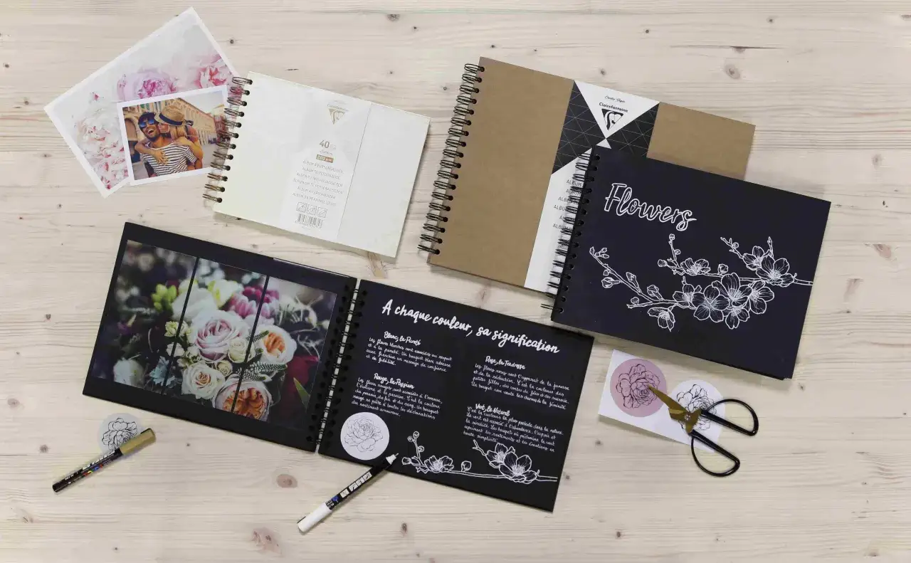Albums photo, photos de couple et de fleurs, stylos et ciseaux sur fond de bois. Une idée art créatif pour vos souvenirs.