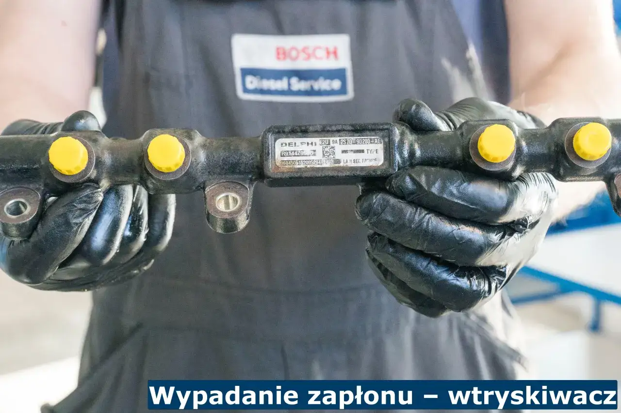 Mechanik w czarnych rękawiczkach trzyma szynę wtryskową Delphi. Może to być przyczyną wypadania zapłonu na 4 cylindrze.