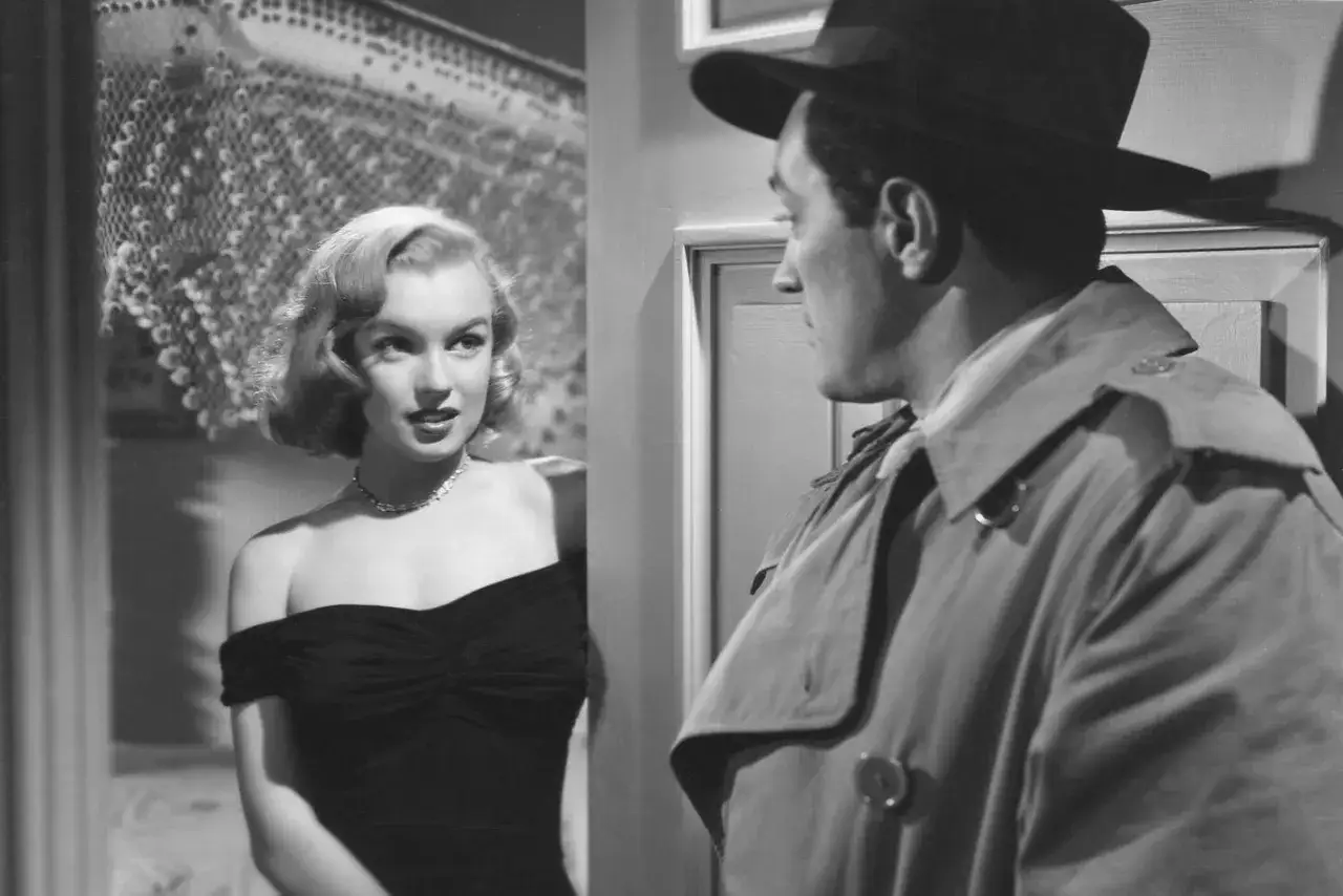 Marilyn Monroe i en svart kl&auml;nning m&ouml;ter en man i trenchcoat och hatt. En klassisk scen fr&aring;n filmer med Marilyn Monroe.