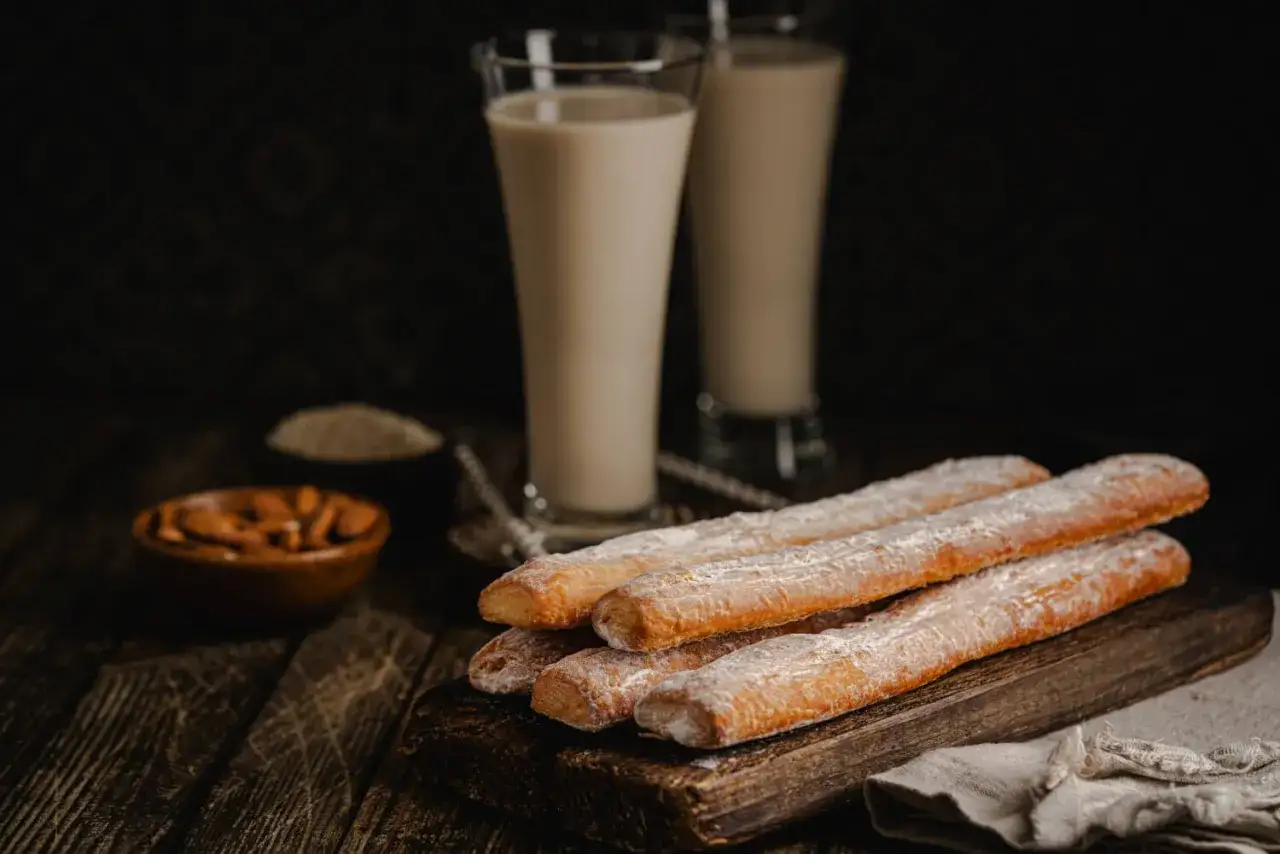 Vasos de horchata, bebida refrescante, junto a churros espolvoreados con az&uacute;car.