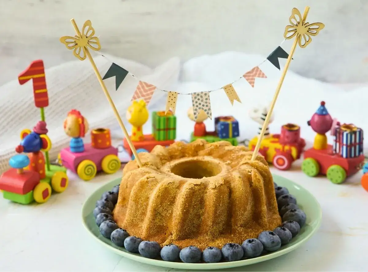 Ein köstlicher Kuchen ohne Zucker, dekoriert mit Blaubeeren und einer bunten Wimpelkette, umgeben von Spielzeugeisenbahnen und einer 