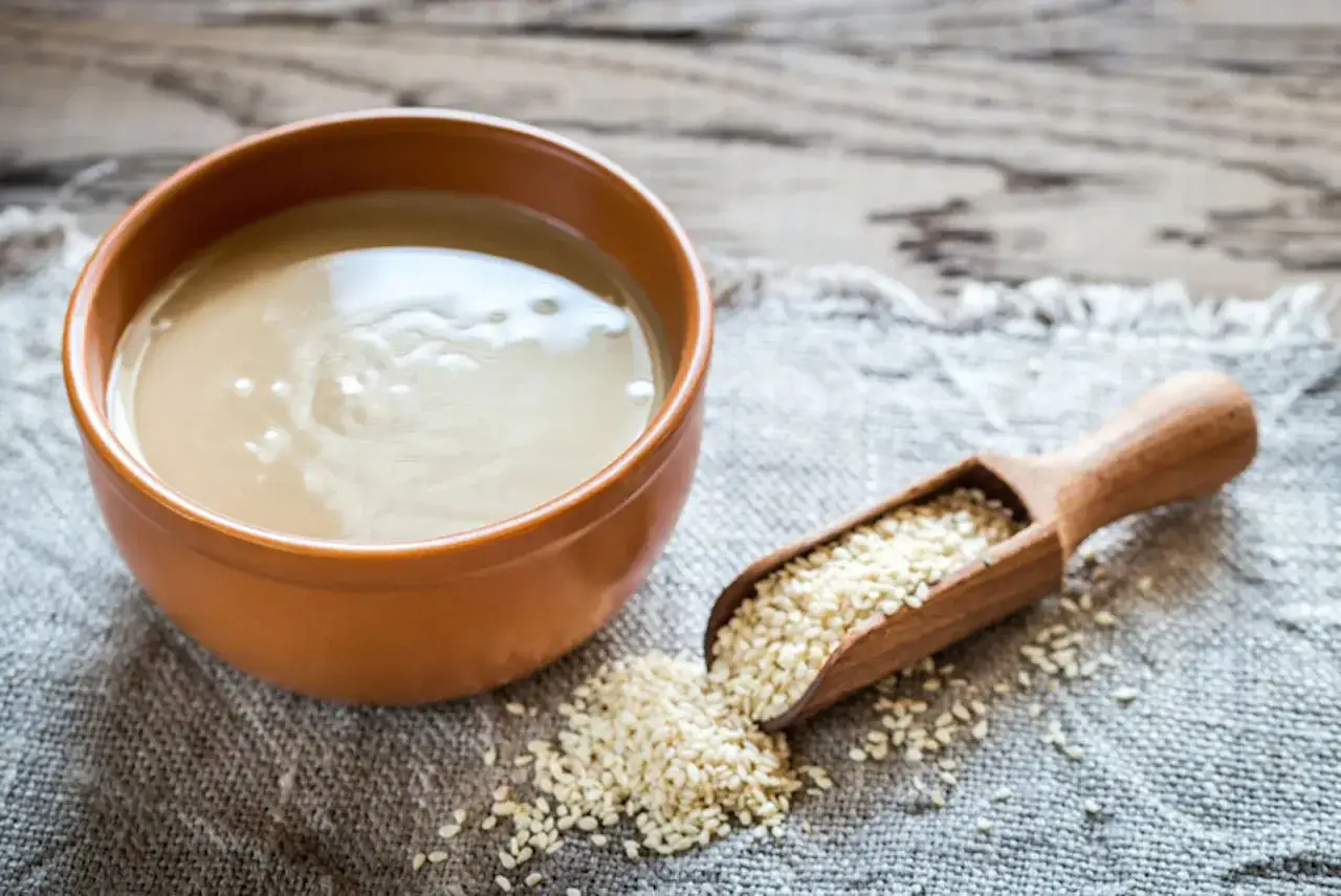 Una ciotola di tahina, crema di sesamo, accanto a un cucchiaio di semi. Cos'è la tahina?