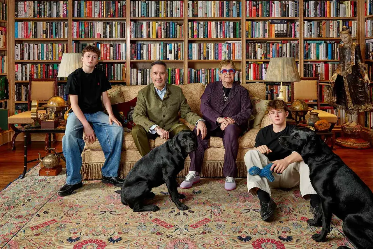 Elton John z rodziną i psami na tle biblioteczki. Dzieci Eltona Johna, Zachary i Elijah, siedzą obok rodziców.