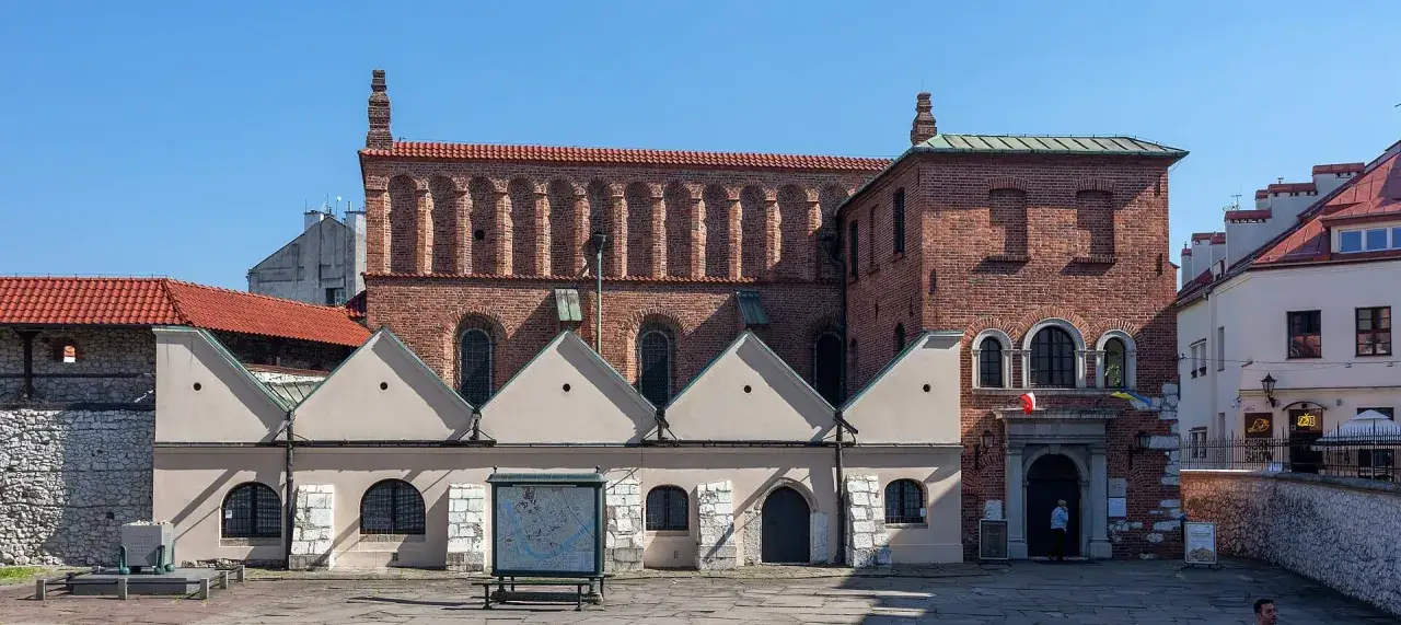 Dawna synagoga w Krakowie, z ceglaną fasadą i charakterystycznymi arkadowymi zdobieniami, stoi dumnie na placu.