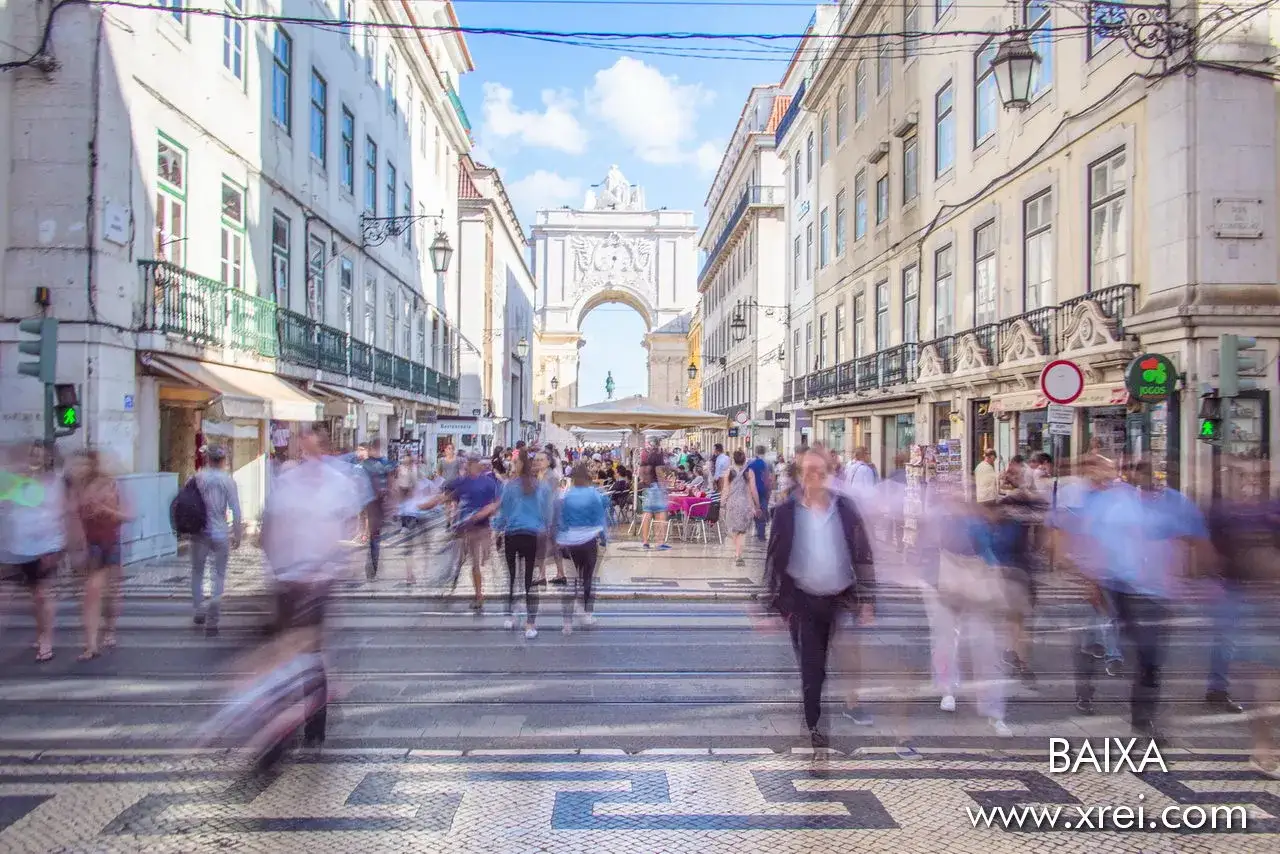 Belebte Stra&szlig;e in Baixa, Lissabon, mit Menschen, die sich im Vordergrund bewegen, und einem Triumphbogen am Ende der Stra&szlig;e.