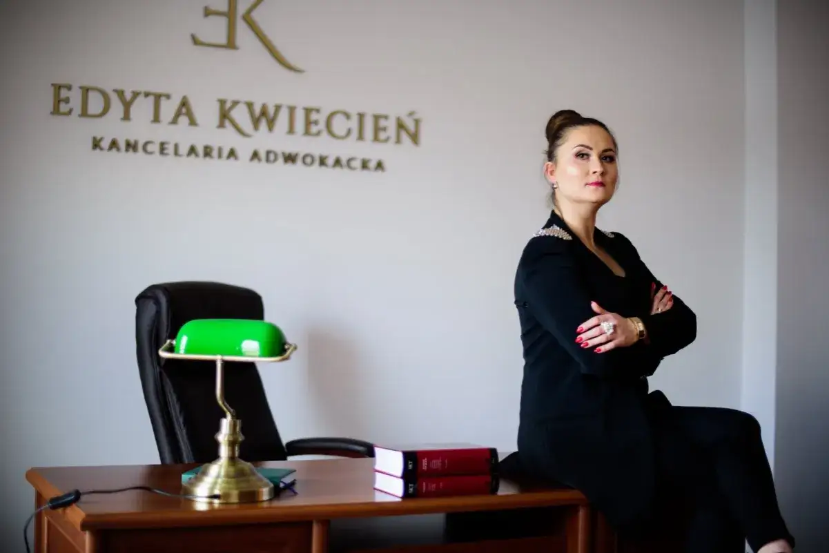 Kobieta w czarnym żakiecie siedzi na biurku w kancelarii, z ramionami skrzyżowanymi.