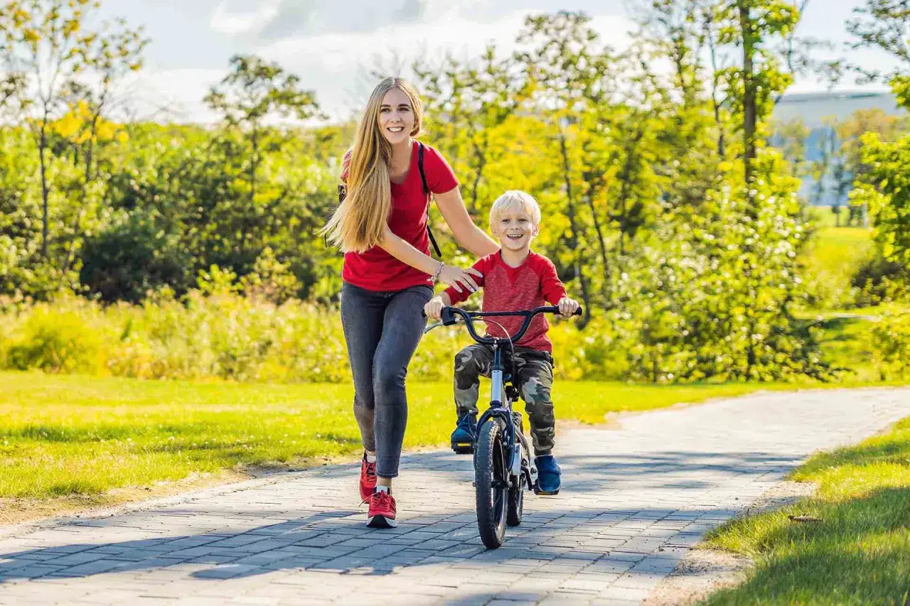 Mama uczy synka, jak nauczyć dziecko jeździć na rowerze. Radosny chłopiec pedałuje, a mama biegnie obok, wspierając go.
