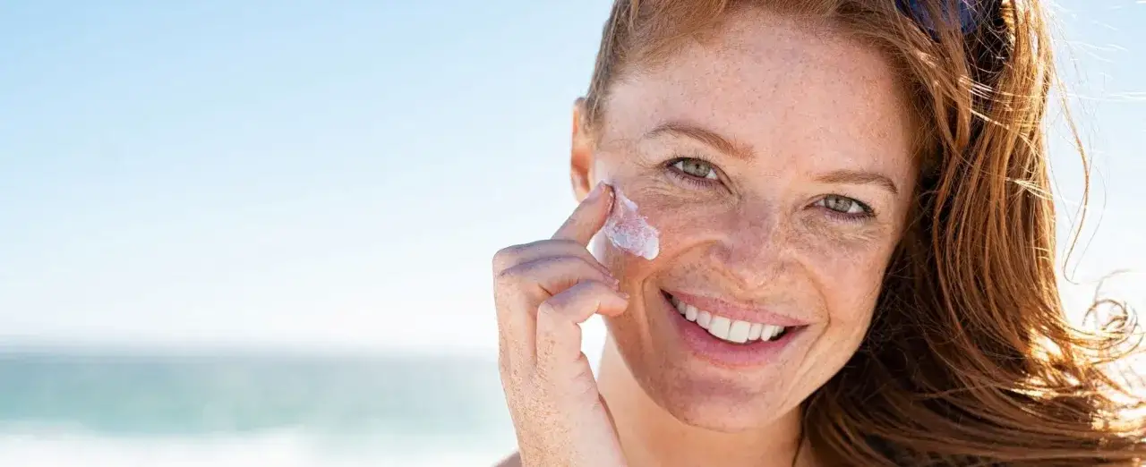 Frau mit Sommersprossen trägt Sonnencreme auf ihr Gesicht auf. Die beste Sonnencreme für reife Haut schützt und pflegt.