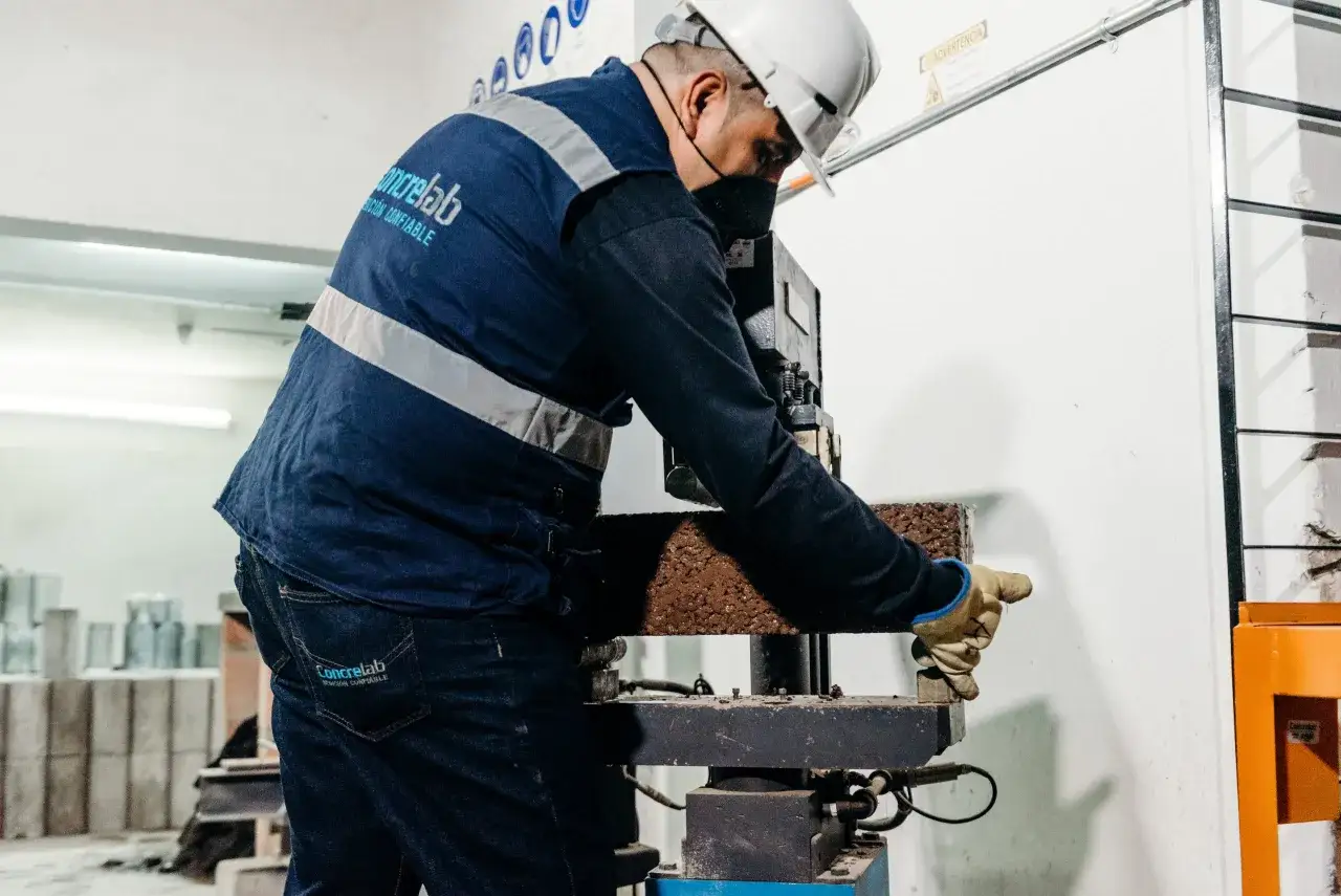 Trabajador con casco y mascarilla prueba la resistencia del hormigón en una máquina.