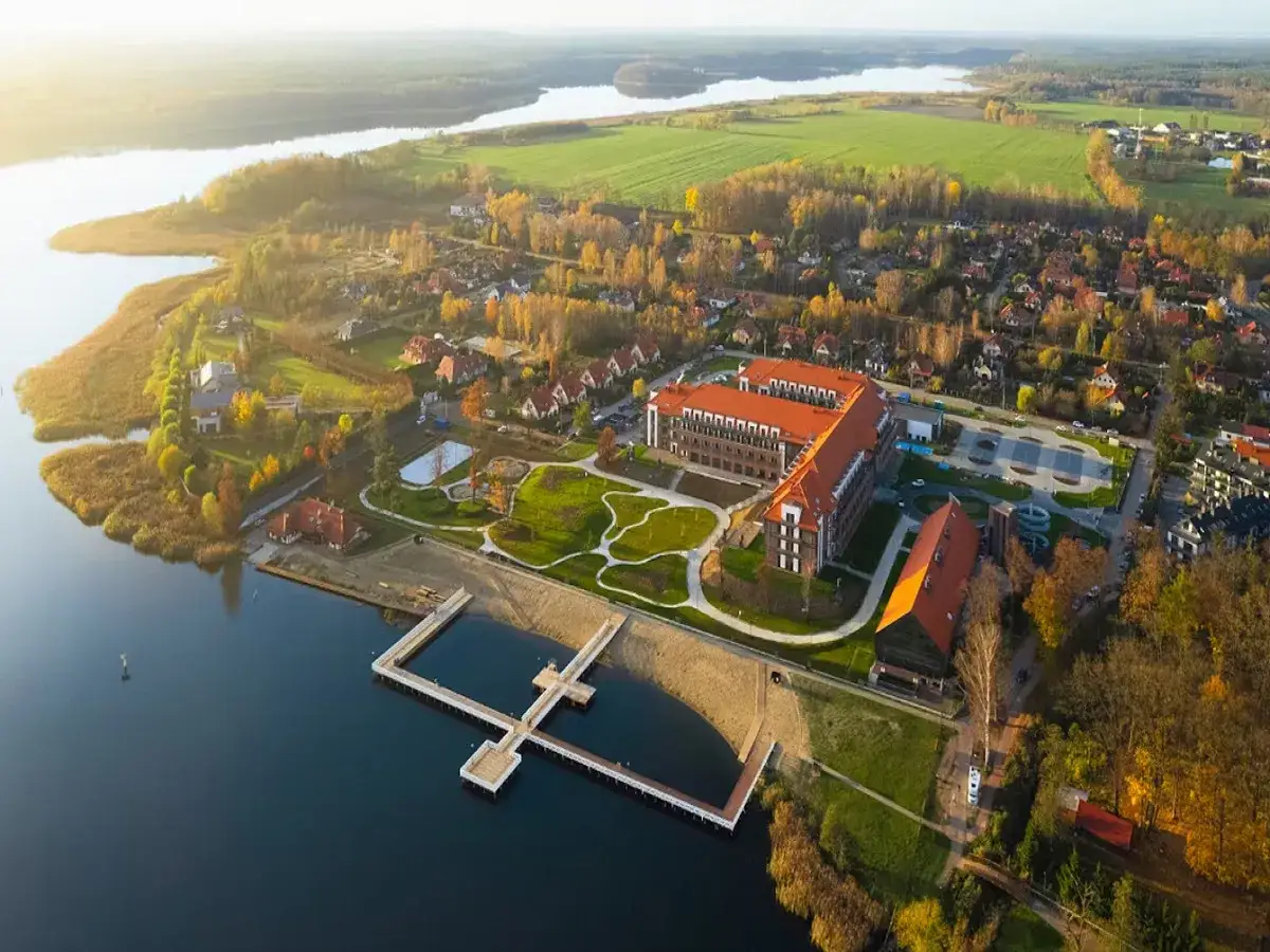 Malowniczy widok na kompleks hotelowy nad jeziorem, z molo i plażą. Idealne miejsce na wypoczynek, jeden z najlepszych hoteli w Polsce.